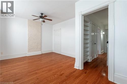 This room features hardwood floors, a white painted brick accent wall, and a ceiling fan - 198 Bay Street N, Hamilton, ON - Indoor Photo Showing Other Room