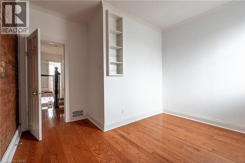 This room features hardwood floors, white walls, and an exposed brick wall - 198 Bay Street N, Hamilton, ON - Indoor Photo Showing Other Room