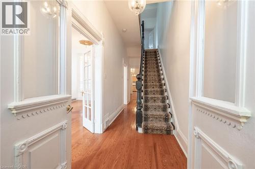 The inviting entry hall features hardwood flooring, a carpeted staircase with a dark wood banister, and an ornate white door - 198 Bay Street N, Hamilton, ON - Indoor Photo Showing Other Room