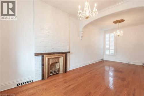Spacious living area featuring hardwood flooring, a decorative fireplace with a brick surround, and a window with white shutters - 198 Bay Street N, Hamilton, ON - Indoor Photo Showing Other Room With Fireplace
