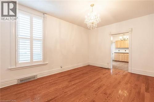 This inviting space features lustrous hardwood floors, a prominent window with white plantation shutters, and an ornate chandelier providing elegant lighting - 198 Bay Street N, Hamilton, ON - Indoor Photo Showing Other Room