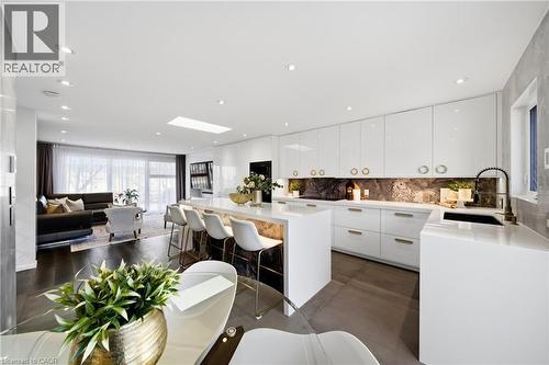 The property features an open-concept living space with dark hardwood flooring, a modern kitchen with white cabinetry, a large kitchen island with seating, and a living area with extensive windows - 2467 Bonner Road, Mississauga, ON - Indoor