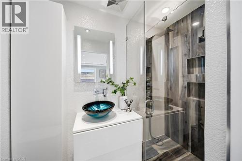 Well-appointed bathroom featuring a modern vanity with a unique vessel sink, an illuminated mirror, and a spacious shower with wood-look tile and built-in niches - 2467 Bonner Road, Mississauga, ON - Indoor