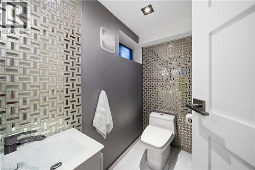 This bathroom features a contemporary design with patterned wall tiling, a modern toilet, and a sleek vanity with a dark faucet - 2467 Bonner Road, Mississauga, ON - Indoor Photo Showing Bathroom