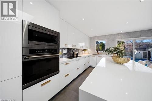 A modern kitchen featuring white cabinetry, a built-in oven and microwave, an expansive island with a light-colored countertop, and a sliding glass door providing natural light - 2467 Bonner Road, Mississauga, ON - Indoor Photo Showing Kitchen