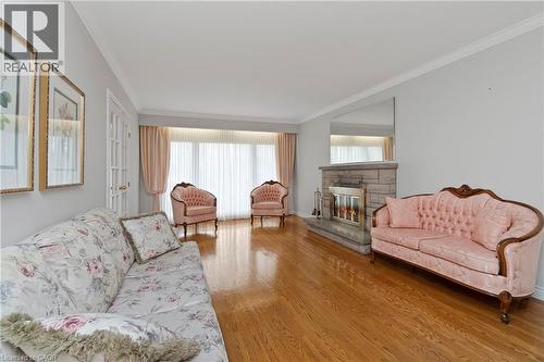 The living room features hardwood flooring, a stone fireplace, and large windows with sheer and solid curtains - 36 Buckingham Drive, Hamilton, ON - Indoor Photo Showing Living Room With Fireplace