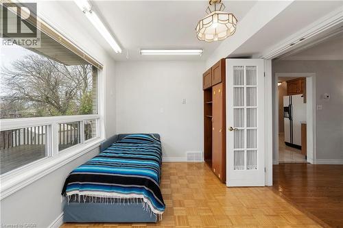 This room features parquet flooring, a large window providing views of the exterior deck and trees, and a classic-style ceiling light fixture - 36 Buckingham Drive, Hamilton, ON - Indoor Photo Showing Bedroom