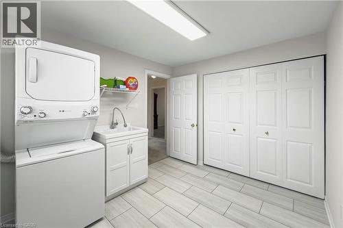 Well-appointed laundry area featuring a stacked washer and dryer, a utility sink with white cabinetry, and extensive built-in storage with bi-fold doors - 36 Buckingham Drive, Hamilton, ON - Indoor Photo Showing Laundry Room