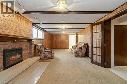 Spacious living area featuring a brick fireplace, wood paneling, and an overhead lighting fixture - 36 Buckingham Drive, Hamilton, ON - Indoor Photo Showing Other Room With Fireplace