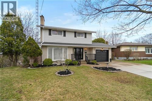 The property features a two-story design with a light-colored brick and siding exterior, a dark gray garage door, and a paved driveway - 36 Buckingham Drive, Hamilton, ON - Outdoor With Facade