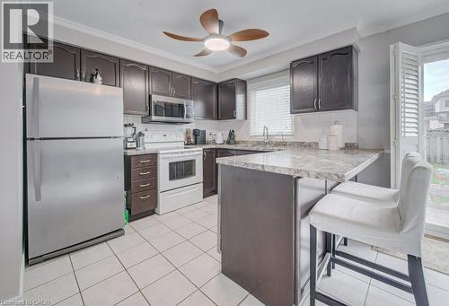 The kitchen features dark wood cabinetry, a white tile floor, and a breakfast bar with a stone-look countertop - 334 Christopher Drive, Cambridge, ON - Indoor Photo Showing Kitchen