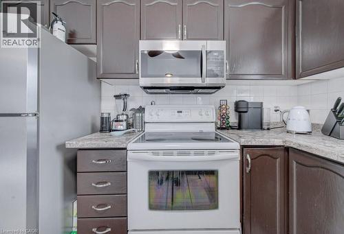 The kitchen features dark wood cabinetry, white appliances, and light-colored countertops with a tiled backsplash - 334 Christopher Drive, Cambridge, ON - Indoor Photo Showing Kitchen
