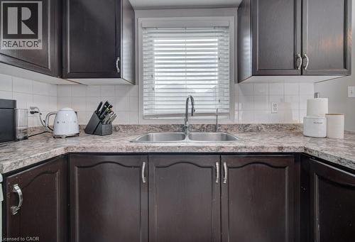 The kitchen features dark wood cabinetry, a double basin stainless steel sink, and a light-colored countertop with a patterned finish - 334 Christopher Drive, Cambridge, ON - Indoor Photo Showing Kitchen With Double Sink