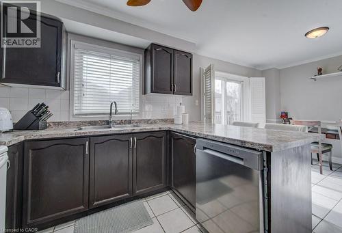 The kitchen features dark cabinetry, light-colored countertops, a stainless steel dishwasher, and a window with blinds above the sink - 334 Christopher Drive, Cambridge, ON - Indoor Photo Showing Kitchen