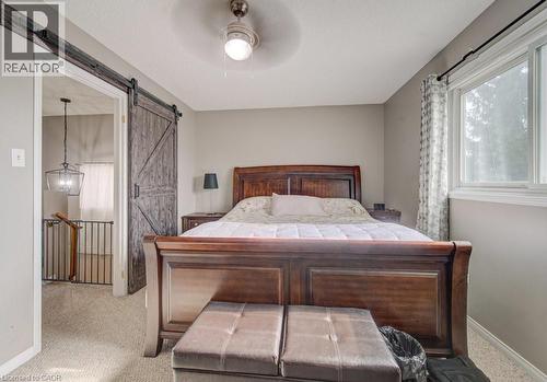 This inviting bedroom features a classic wooden bed frame, a barn door, and a ceiling fan - 334 Christopher Drive, Cambridge, ON - Indoor Photo Showing Bedroom