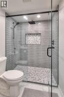 The bathroom features a spacious shower with glass enclosure, textured tile walls, a built-in shower niche, and a contrasting tile floor - 