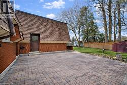 The property features extensive brickwork, a brown shingled roof, and a paved patio area - 