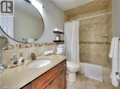 Bathroom featuring a vanity with a light-colored countertop, a round mirror, and a bathtub with tiled walls - 42 Culpepper Drive, Waterloo, ON - Indoor Photo Showing Bathroom
