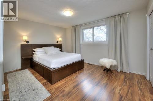 This inviting room features warm-toned hardwood flooring, a window with curtains for natural light, and a built-in bed frame with an integrated headboard and side shelves - 42 Culpepper Drive, Waterloo, ON - Indoor Photo Showing Bedroom