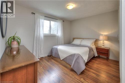 This room features warm hardwood flooring, a window with sheer curtains, and a ceiling-mounted light fixture - 42 Culpepper Drive, Waterloo, ON - Indoor Photo Showing Bedroom