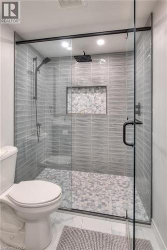 The bathroom features a spacious shower with glass enclosure, textured tile walls, a built-in shower niche, and a contrasting tile floor - 42 Culpepper Drive, Waterloo, ON - Indoor Photo Showing Bathroom