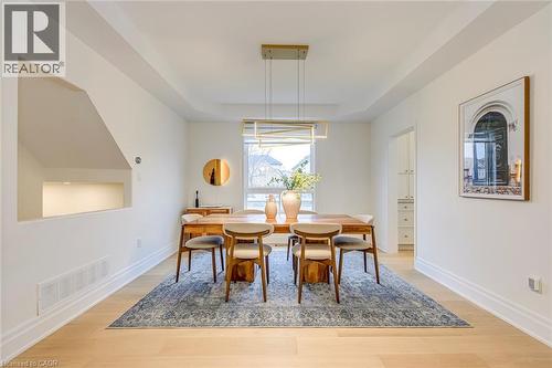 The dining area features light-toned hardwood flooring, a tray ceiling, and a large window providing natural light - 4267 Sarazen Drive, Burlington, ON - Indoor Photo Showing Dining Room