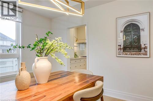 The dining area features light hardwood flooring, a modern linear chandelier, and a substantial wooden dining table - 4267 Sarazen Drive, Burlington, ON - Indoor