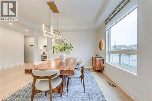 Dining area featuring hardwood floors, a large window providing natural light, and a modern rectangular chandelier - 4267 Sarazen Drive, Burlington, ON - Indoor Photo Showing Dining Room