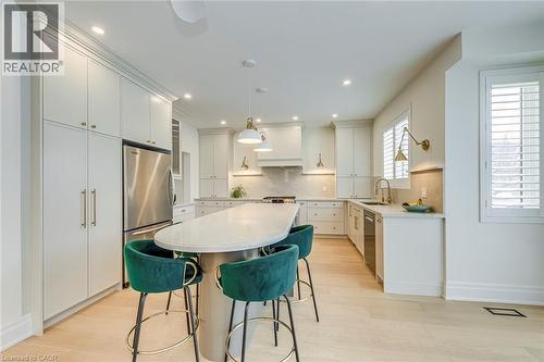 The kitchen showcases light-toned flooring, extensive white cabinetry with gold-toned hardware, a central island with a light-colored countertop, and stainless steel appliances - 4267 Sarazen Drive, Burlington, ON - Indoor