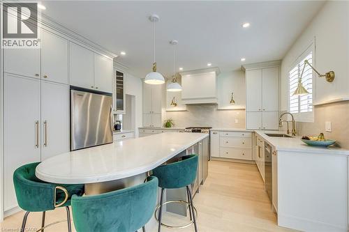 The kitchen features light wood flooring, white cabinetry, a large kitchen island with a white countertop, and stainless steel appliances including a refrigerator and dishwasher - 4267 Sarazen Drive, Burlington, ON - Indoor Photo Showing Kitchen With Upgraded Kitchen