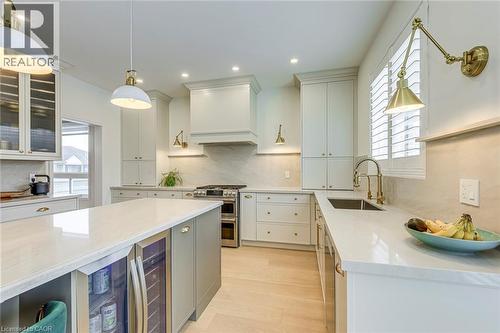 This kitchen showcases light-toned cabinetry, an island with a built-in beverage cooler, a double oven range, and light wood flooring - 4267 Sarazen Drive, Burlington, ON - Indoor Photo Showing Kitchen With Upgraded Kitchen