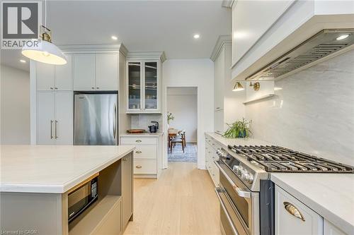 The kitchen features an island with a built-in microwave, light-colored flooring, and extensive cabinetry, including a glass-front cabinet - 4267 Sarazen Drive, Burlington, ON - Indoor Photo Showing Kitchen With Upgraded Kitchen
