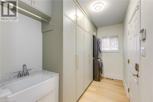 The laundry area features a built-in sink with a marble countertop, overhead cabinetry, and light wood flooring - 4267 Sarazen Drive, Burlington, ON - Indoor Photo Showing Laundry Room