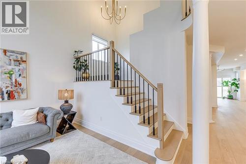 This bright interior features a grand staircase with light wood treads and a black metal railing, complemented by hardwood floors - 4267 Sarazen Drive, Burlington, ON - Indoor