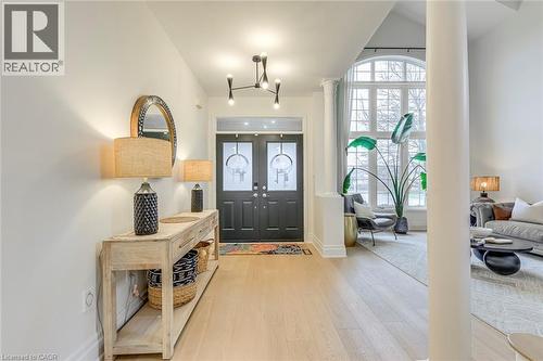 Elegant entryway featuring light hardwood floors, a modern chandelier, and double dark doors with glass inserts - 4267 Sarazen Drive, Burlington, ON - Indoor Photo Showing Other Room