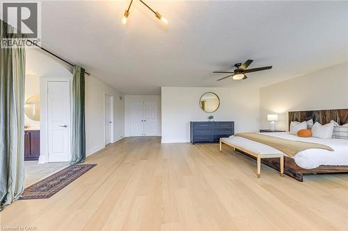 The property features light-toned hardwood flooring, a ceiling fan, and a light fixture with three exposed bulbs - 4267 Sarazen Drive, Burlington, ON - Indoor Photo Showing Bedroom