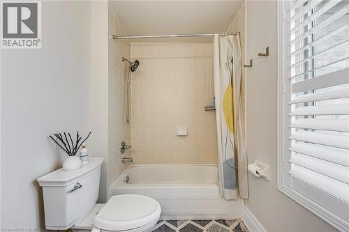 The bathroom features a bathtub with a tiled shower surround, a toilet, and a window with white shutters - 4267 Sarazen Drive, Burlington, ON - Indoor Photo Showing Bathroom