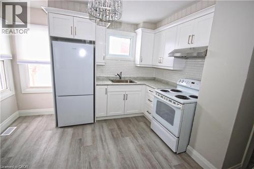 The kitchen features white cabinetry, light-colored countertops, a white refrigerator, and a white electric range with a stainless steel hood fan - 1356 Upper Wellington Street, Hamilton, ON - Indoor Photo Showing Kitchen