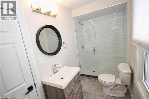 Contemporary bathroom featuring a vanity with a rectangular sink, a circular mirror, and a glass-enclosed shower with subway tile - 1356 Upper Wellington Street, Hamilton, ON - Indoor Photo Showing Bathroom