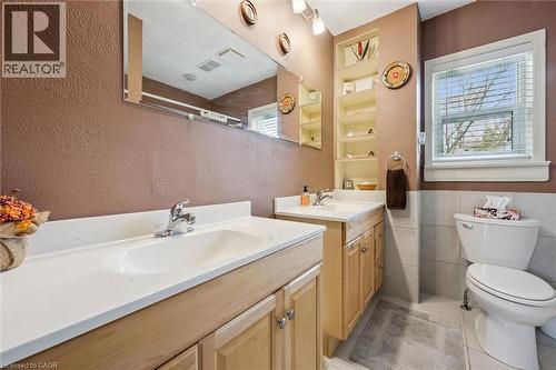 This bathroom features dual vanity sinks with light wood cabinetry, a large mirror, built-in shelving, and a window providing natural light - 155 Hungerford Road, Cambridge, ON - Indoor Photo Showing Bathroom