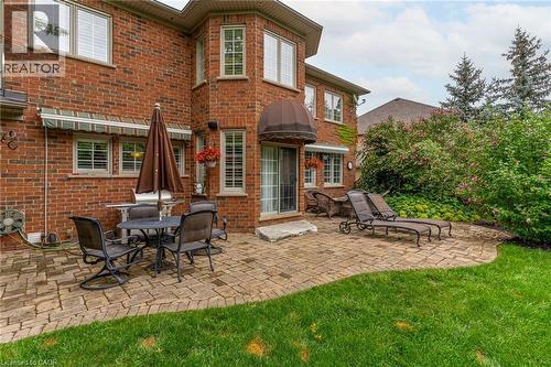 This property features an expansive brick exterior with numerous windows, complemented by a paver patio and a lush green lawn - 4278 Clubview Drive, Burlington, ON - Outdoor With Deck Patio Veranda