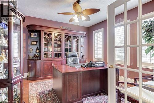 This dedicated office space features hardwood floors, a ceiling fan, and built-in wooden cabinetry with glass doors - 4278 Clubview Drive, Burlington, ON - Indoor Photo Showing Office