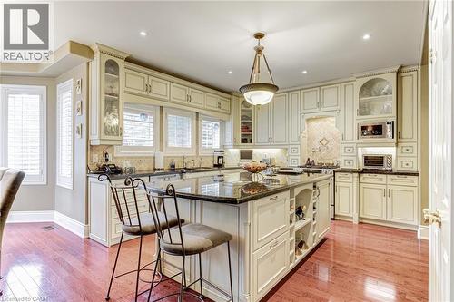 This kitchen features extensive cabinetry, a central island with bar seating, and richly toned hardwood flooring - 4278 Clubview Drive, Burlington, ON - Indoor Photo Showing Other Room