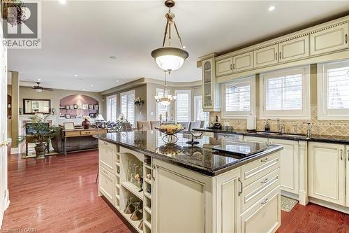 The kitchen features a large island with a dark granite countertop, light-colored cabinetry with decorative molding, and a tiled backsplash - 4278 Clubview Drive, Burlington, ON - Indoor Photo Showing Kitchen With Upgraded Kitchen