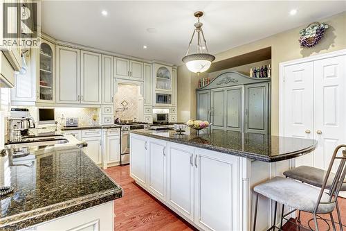 The kitchen features an expansive island with a dark granite countertop, white cabinetry, and hardwood flooring - 4278 Clubview Drive, Burlington, ON - Indoor Photo Showing Kitchen