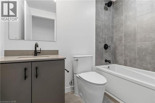 The bathroom features a vanity with a countertop and a black faucet, a white toilet, and a bathtub with a tiled shower surround - 4878 Powers Common Unit# 224, Burlington, ON - Indoor Photo Showing Bathroom