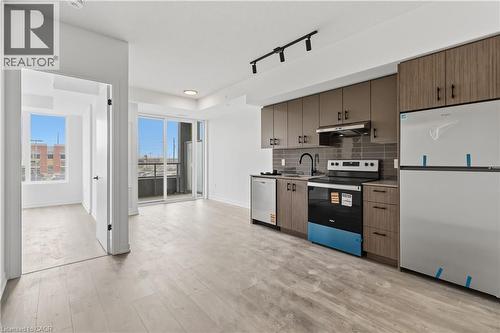 Open concept living area featuring light-toned flooring, a modern kitchen with integrated appliances, and a sliding glass door leading to a balcony - 4878 Powers Common Unit# 224, Burlington, ON - Indoor Photo Showing Kitchen