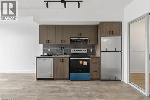 The kitchen features modern cabinetry, a grey subway tile backsplash, a stainless steel dishwasher, a black range, and a stainless steel refrigerator - 4878 Powers Common Unit# 224, Burlington, ON - Indoor Photo Showing Kitchen