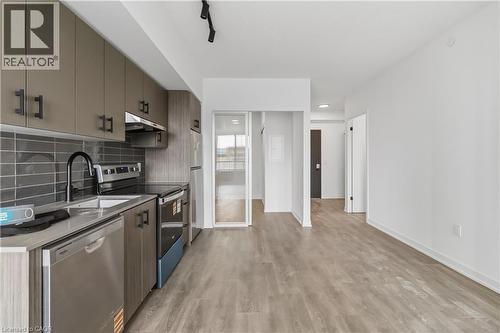 The property features a kitchen with neutral-toned cabinetry, stainless steel appliances, and a dark subway tile backsplash - 4878 Powers Common Unit# 224, Burlington, ON - Indoor Photo Showing Kitchen