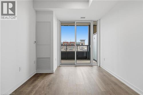This inviting space features light wood-style flooring, white walls, and a sliding glass door leading to a balcony - 4878 Powers Common Unit# 224, Burlington, ON - Indoor Photo Showing Other Room